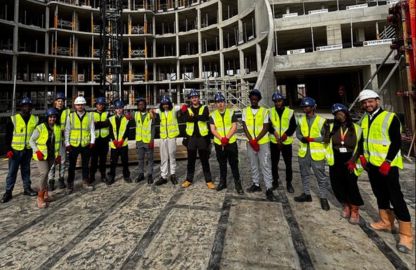 London South Bank Technical College plumbing student wearing yellow vests stands in front of a building: the Oval Village, engaged in conversation