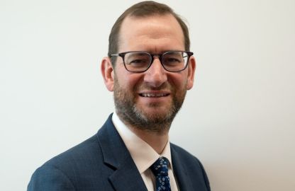 A smiling man wearing glasses and a tie, exuding a friendly and professional demeanor.