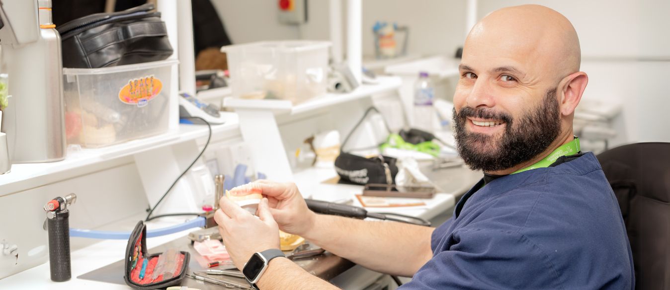 A smiling man with a beard works on a tooth, showcasing his focus and expertise in dental care.